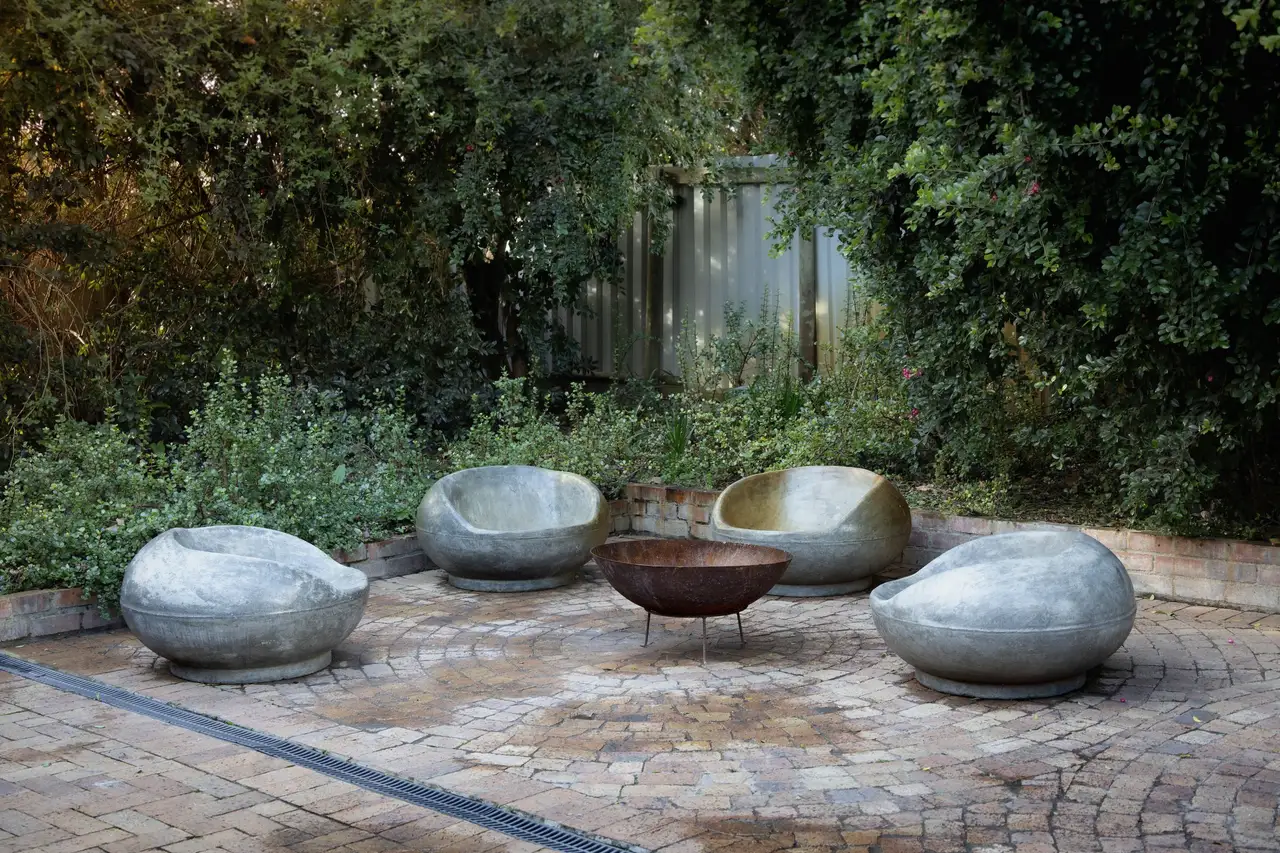 Circular brick terrace with four stone seats around a steel fire bowl, backed by dense evergreen planting