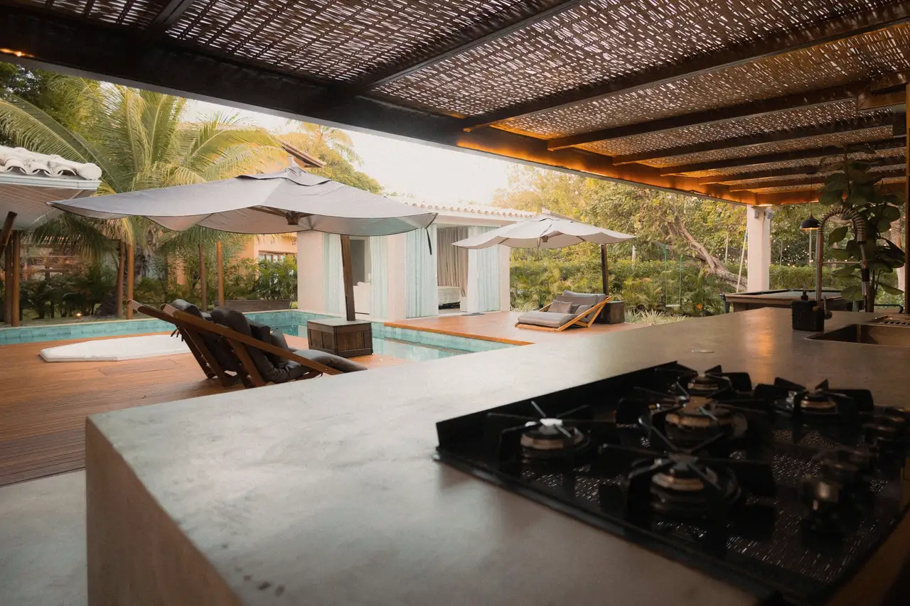 Covered outdoor kitchen with a stone counter and built-in cooktop in the evening