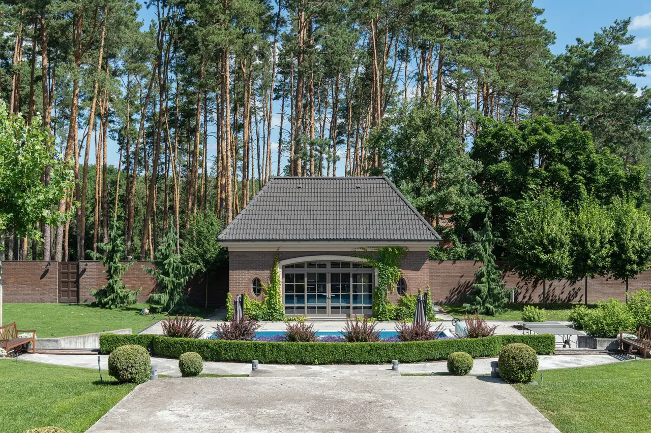 Pool behind a clipped hedge with a brick pool house under tall pines